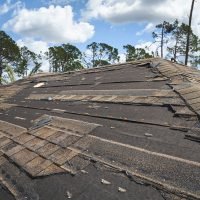 Damaged house roof with missing shingles after hurricane Ian in Florida. Consequences of natural disaster.